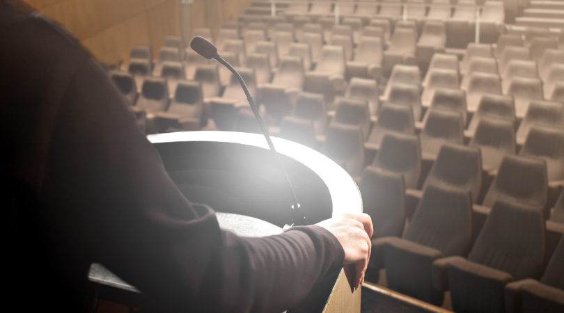 person on stage in front of empty chairs