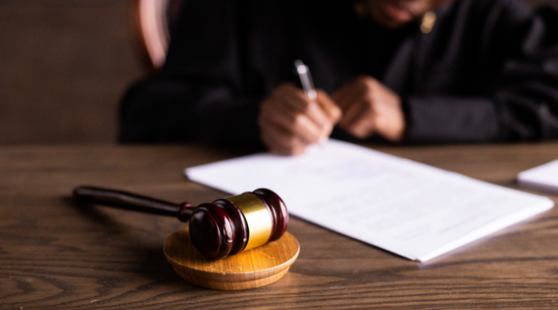 person writing on a paper with a pen in the background with a gavel on a table in focus